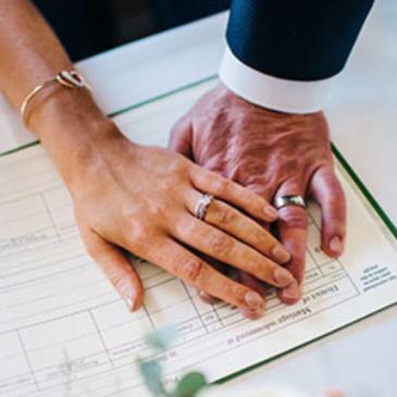 Bride and groom holding hands while signing a marriage certificate.