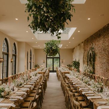 Long hall with hanging floral baskets and tables and chairs laid out for a wedding dinner.