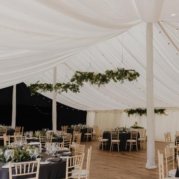 Marquee with fairy lights and tables and chairs set for dinner. 