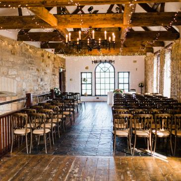 Indoor area with fairy lights and chairs lined up facing towards wedding ceremony.