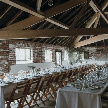 Long tables with seats each side laid out for a wedding dinner.