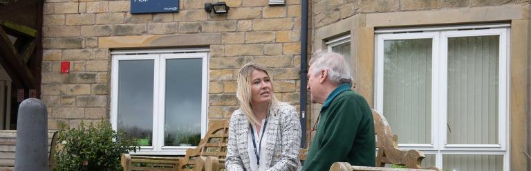 Two people sat on a bench outside an extra care building