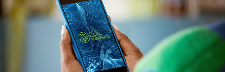 A person holding a mobile phone showing the Active North Yorkshire app loading screen