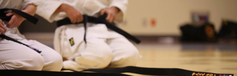 A child in a karate gi sitting in front of a black belt