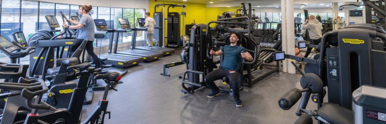 A man lifting weights and a woman on a treadmill among the gym equipment at Pateley Bridge Leisure and Wellbeing Hub