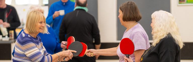A group of women with table tennis paddles getting ready to play at Stockwell Community Wellbeing Hub.