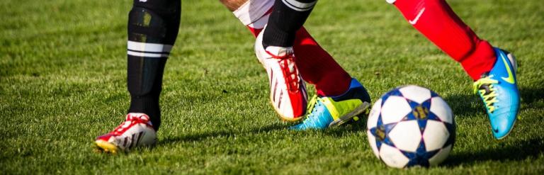 Two players challenging for a ball on football pitch, shown from the knees down.