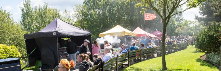 Groups of people sitting and standing in the sunshine around the food tents