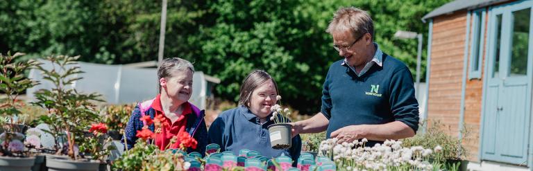 Three adults smiling behind a table full of plants in pots