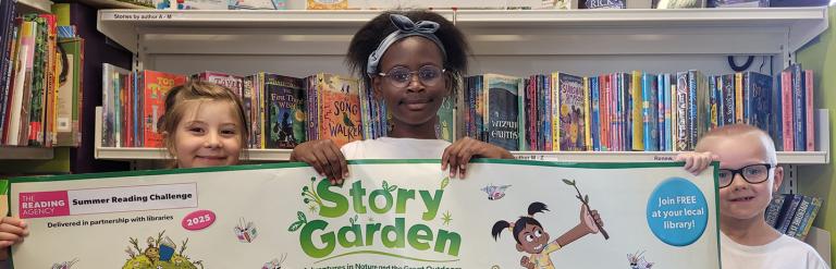 Three children smiling holding a Story Garden banner