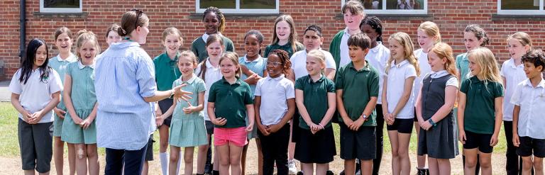 Group of children standing together outside facing their teacher