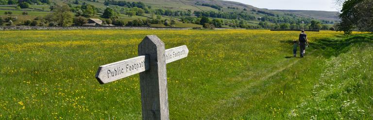 Public footpath sign and two people working in the Dales on a bright day