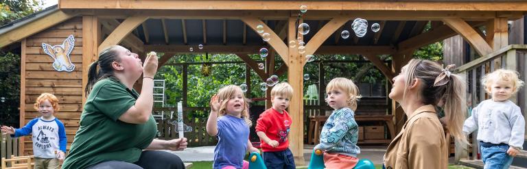 Group of nursery children and two adults playing with bubbles outside