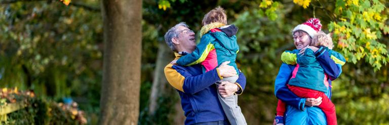 Two adults walking outside on an autumn day carrying two young children