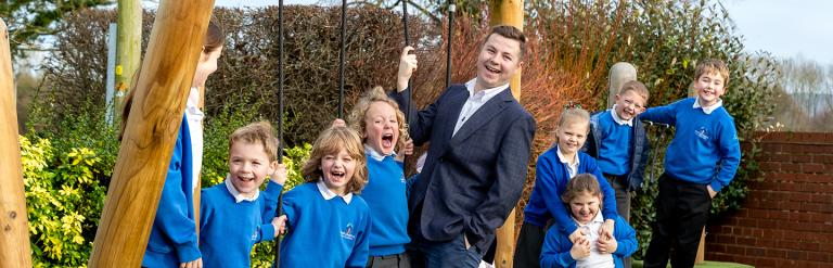 Teacher, Ben McAuley and several school children on wooden playground equipment