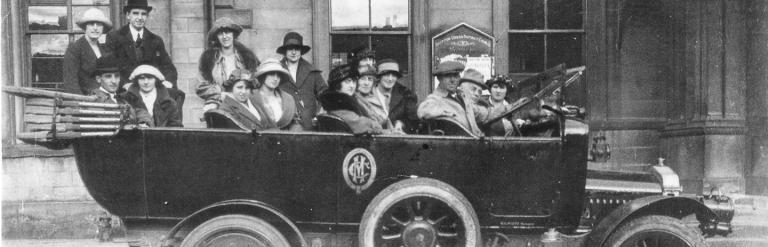 Black and white photo of a motor vehicle carrying a large group of people