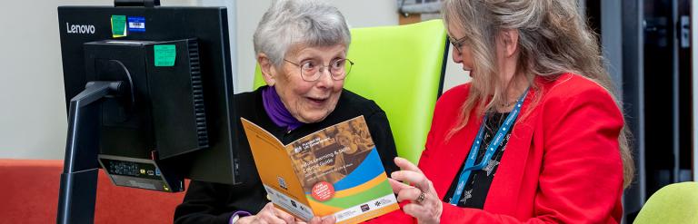 Two adults sitting at a desk reading a booklet