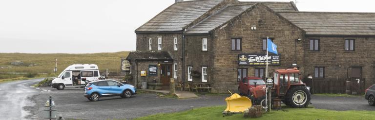 External of Tan Hill inn with a red tractor and vehicles