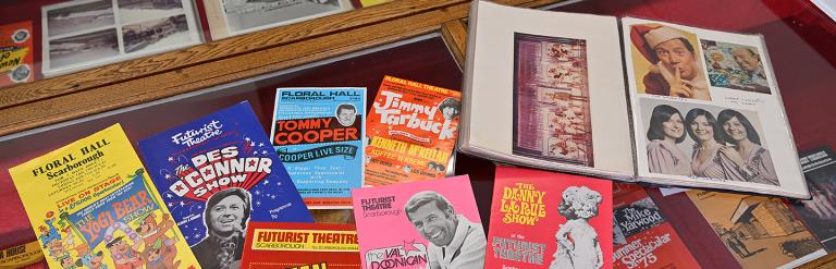 A selection of bright past programmes and flyers displayed on a glass cabinet