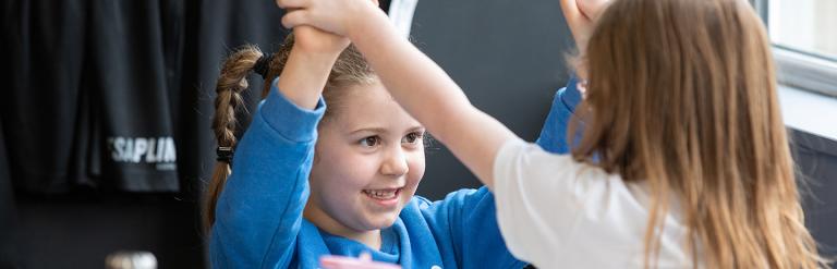Two children holding hands above their hands while sitting at a table
