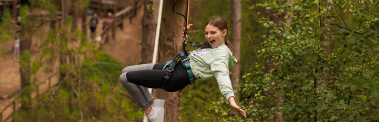 Child in a harness leaning back on a rope high in the trees