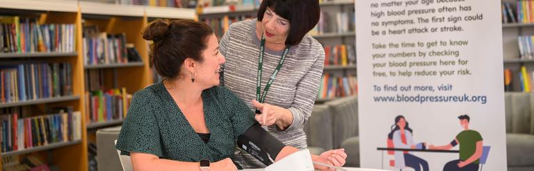 wo people in a library next to a blood pressure station banner 