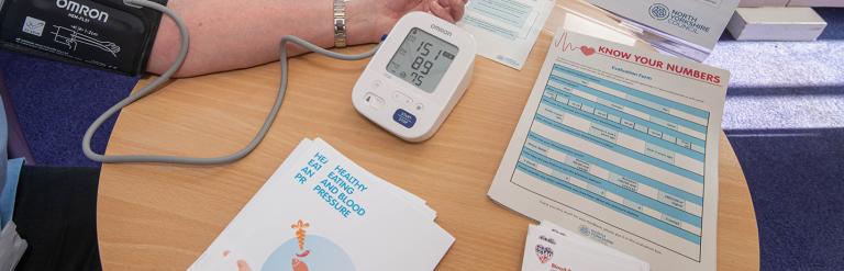 Adult sitting at a wooden table having their blood pressure taken