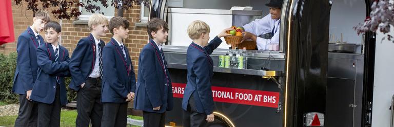 Group of children in the school uniform queue for fruit at their school food van